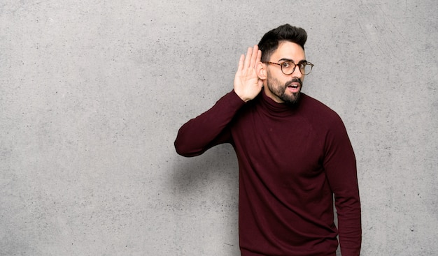 Handsome man with glasses listening to something by putting hand on the ear 