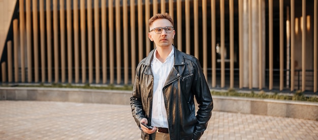 Handsome man with glasses with a smartphone on the street of a big city. Businessman talking on the phone on urban background