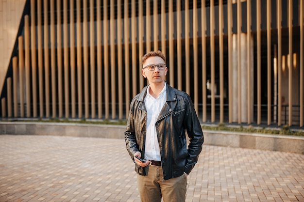 Handsome man with glasses with a smartphone on the street of a big city. Businessman talking on the phone on urban background