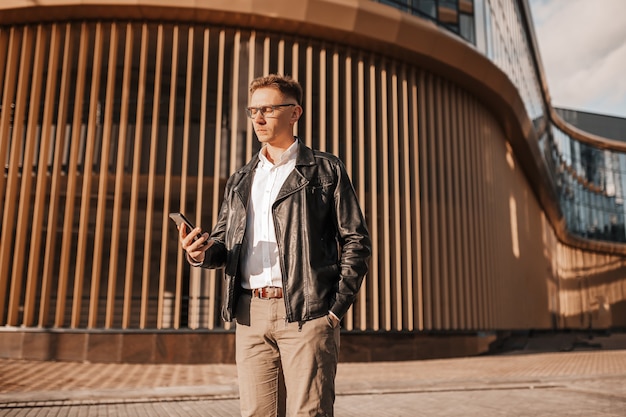 Handsome man with glasses with a smartphone on the street of a big city. Businessman talking on the phone on urban background