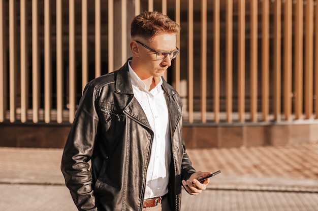 Handsome man with glasses with a smartphone on the street of a big city. Businessman talking on the phone on urban background