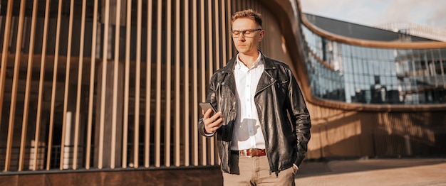 Handsome man with glasses with a smartphone on the street of a big city. Businessman talking on the phone on urban background