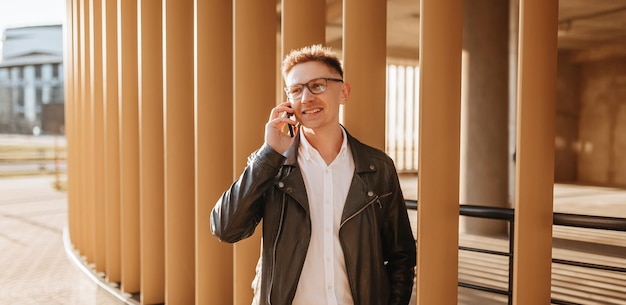 Handsome man with glasses with a smartphone on the street of a big city Businessman talking on the phone on urban background