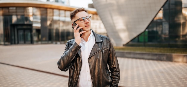 Handsome man with glasses with a smartphone on the street of a big city Businessman talking on the phone on urban background