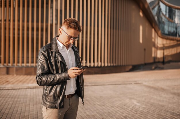 Handsome man with glasses with a smartphone on the street of a big city Businessman talking on the phone on urban background