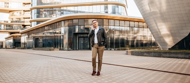 Handsome man with glasses with a smartphone on the street of a big city Businessman talking on the phone on urban background