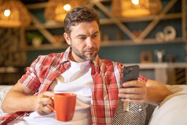 Handsome man with mobile phone sitting at home american man using phone while sitting on sofa at liv