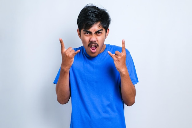 Handsome man with mustache wearing casual shirt over white background shouting with crazy expression doing rock symbol with hands up. Music star. Heavy metal concept.