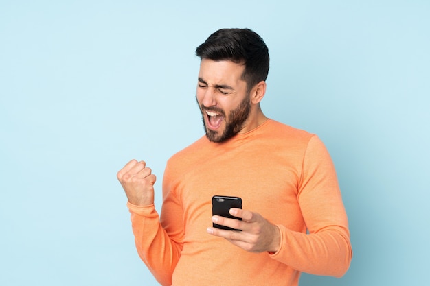 handsome man with phone in victory position over blue