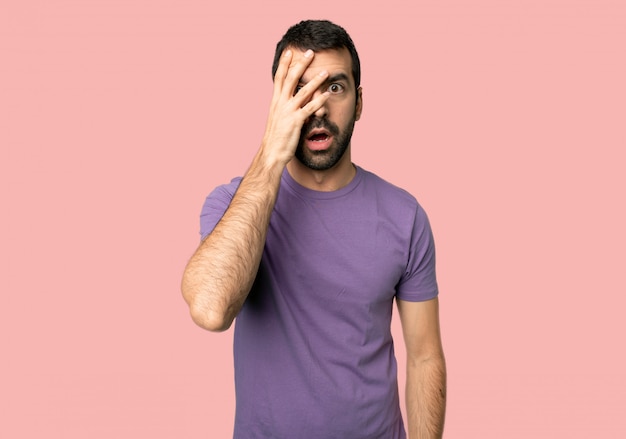 Handsome man with surprise and shocked facial expression on isolated pink background