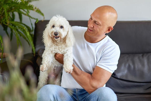 Handsome man with white dog at home on sofa