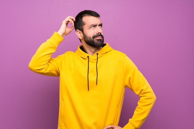 Handsome man with yellow sweatshirt having doubts while scratching head