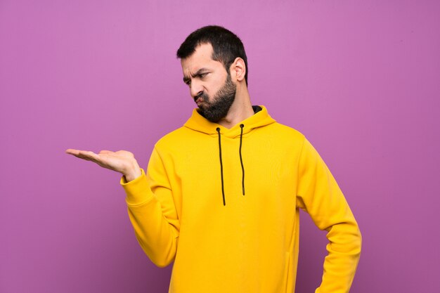 Handsome man with yellow sweatshirt holding copyspace with doubts