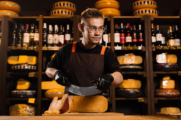 Handsome man worker of cheese shop cut limited gouda with knife Cheese sommelier working in cheese shop Creative ideas for advertising cheese products