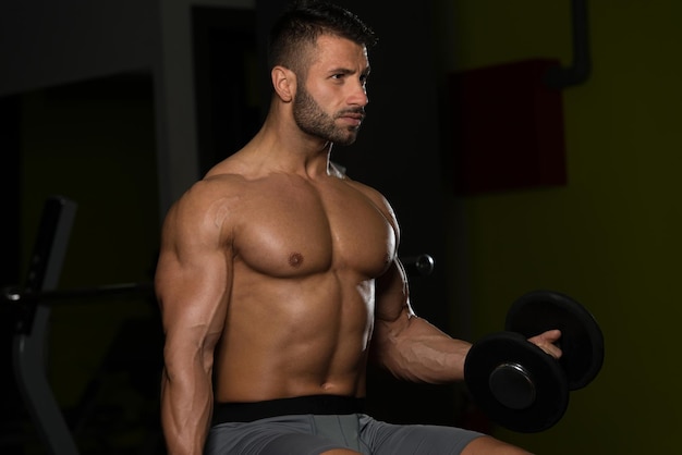 Handsome Man Working Out Biceps In A Dark Gym  Dumbbell Concentration Curls