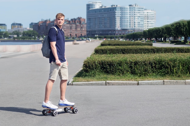 Handsome man, young guy on a modern electric skateboard or longboard riding in the city with backpack at summer day. Technology, gadget, transport concept.