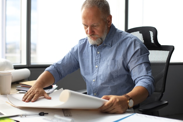 Handsome mature business man using blueprint while working in the modern working space.