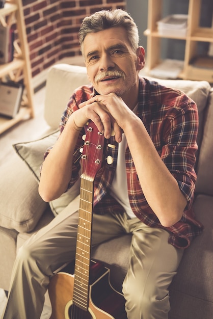 Handsome mature man in casual clothes is holding a guitar.