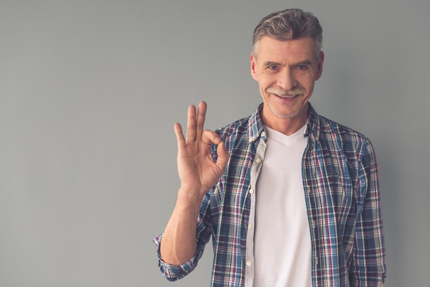 Handsome mature man in casual wear is showing Ok sign