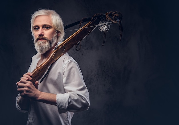 Handsome mature man with a gray beard and white shirt holding a crossbow on shoulder