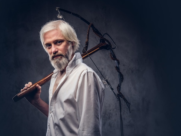 Handsome mature man with a gray beard and white shirt holding a crossbow on shoulder