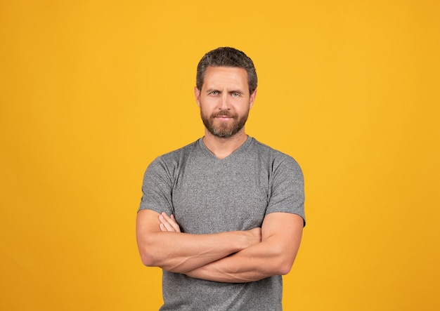 Handsome mature muscular man with beard smiling on yellow background crossed hands, male beauty.