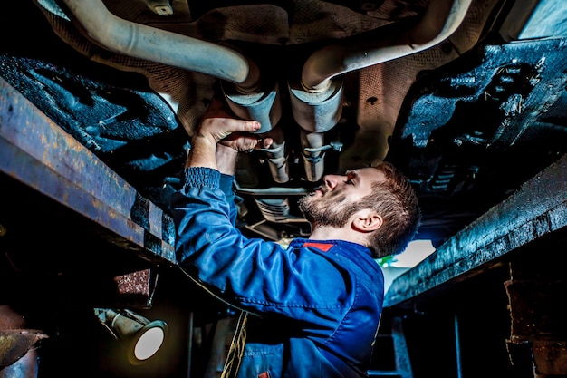 Handsome mechanic in uniform are working in auto service with lifted vehicle. 