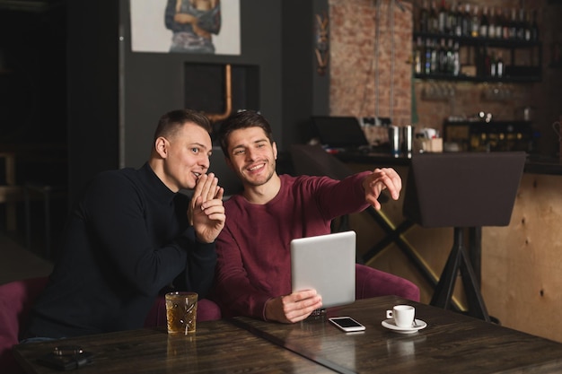 Handsome men using digital tablet and pointing away while having rest at the bar, copy space