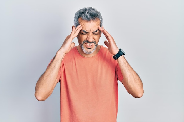 Handsome middle age man with grey hair wearing casual t shirt with hand on head for pain in head because stress. suffering migraine.