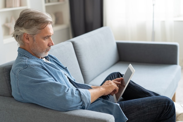 Handsome middle aged businessman is using a laptop and smiling while working at home.