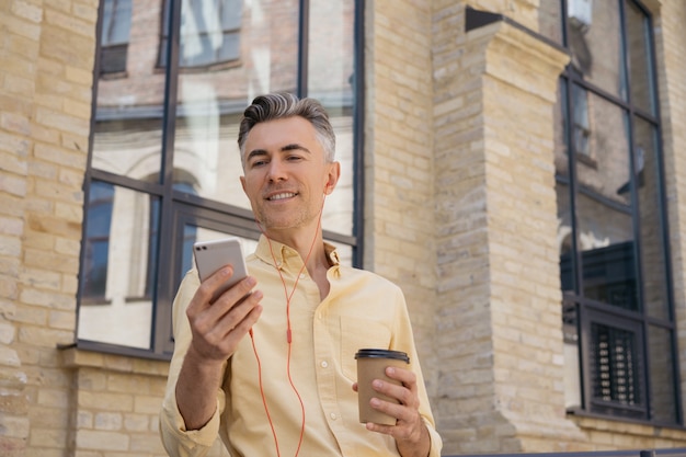 Handsome middle aged man holding mobile phone, drinking coffee, reading news