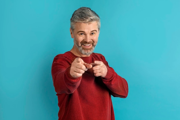 Handsome middle aged man pointing at camera isolated on blue