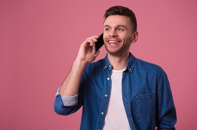 Handsome modern casual man is talking on smart phone isolated on pink background