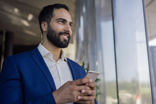 Handsome moroccan businessman using mobile phone shopping online looking at window in modern office