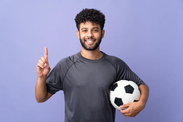 Handsome Moroccan young football player man over isolated on purple wall showing and lifting a finger in sign of the best