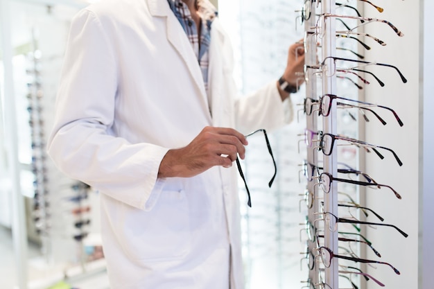 Handsome ophthalmologist choosing eyeglasses frame for his client in optical store. Selective focus on hand.