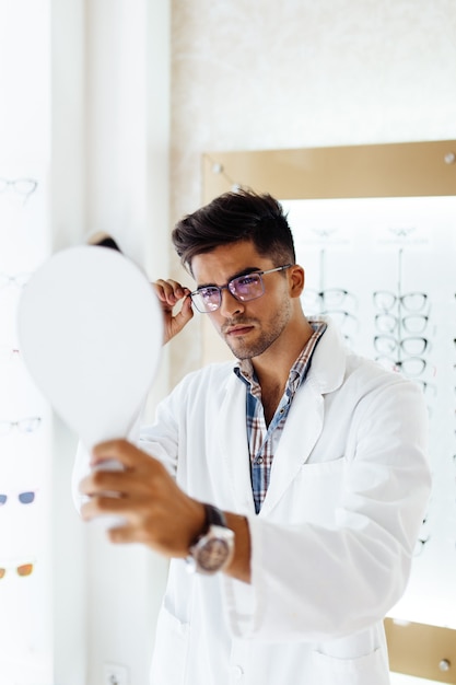 Handsome ophthalmologist choosing eyeglasses frame for his client in optical store.