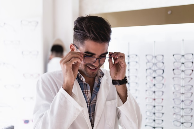 Handsome ophthalmologist choosing eyeglasses frame for his client in optical store.