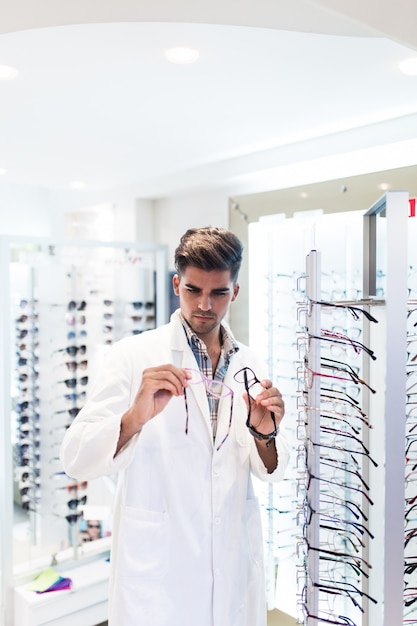 Handsome ophthalmologist holding eyeglasses frame in optical store.