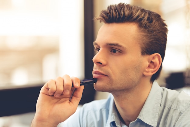 Handsome pensive young businessman is holding a pen.