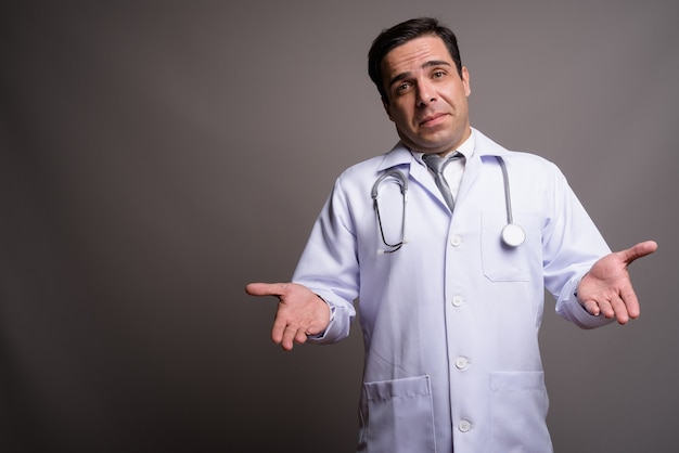 Handsome Persian man doctor against gray wall