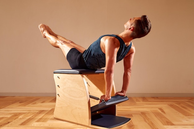 Handsome pilates male instructor performing stretching balance fitness exercise on small barrel equipment at the pilates studio modern onterior indoor