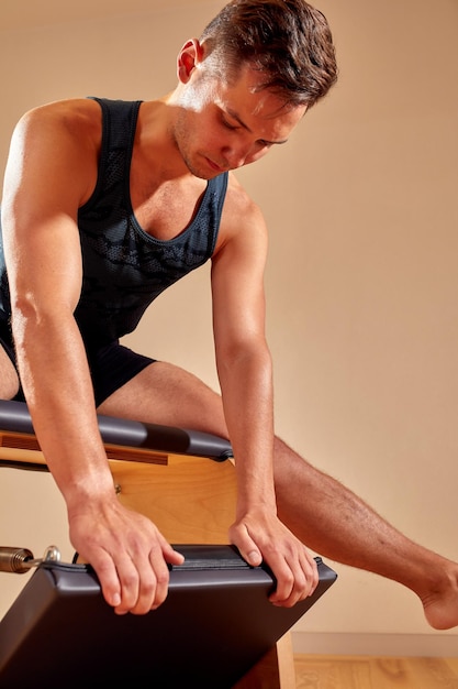 Handsome pilates male instructor performing stretching balance fitness exercise on small barrel equipment at the pilates studio modern onterior indoor