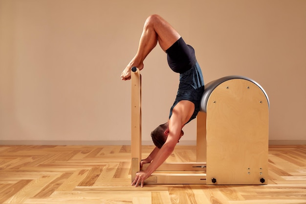 Handsome pilates male instructor performing stretching balance fitness exercise on small barrel equipment at the pilates studio modern onterior indoor