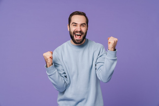 a handsome positive happy young man isolated over purple wall showing winner gesture.