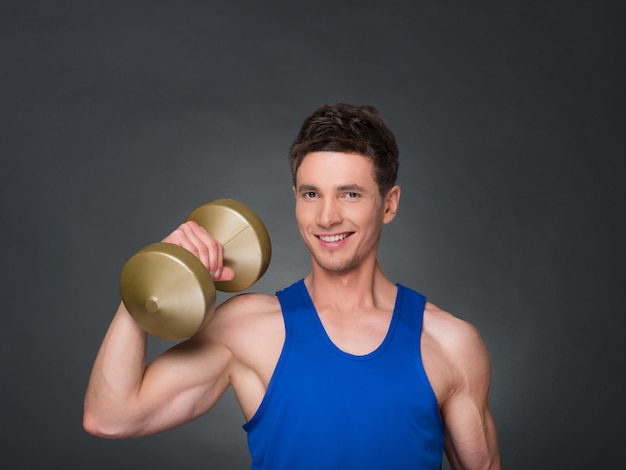 Handsome power athletic man in training pumping up muscles with dumbbells in a gym. blue t-shirt