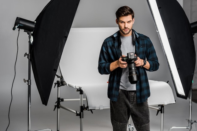 Handsome professional young photographer using camera in photo studio