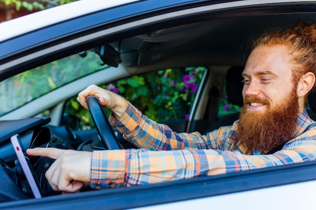 Handsome redhaired ginger man with long beard going on trip during summer vacation on new car