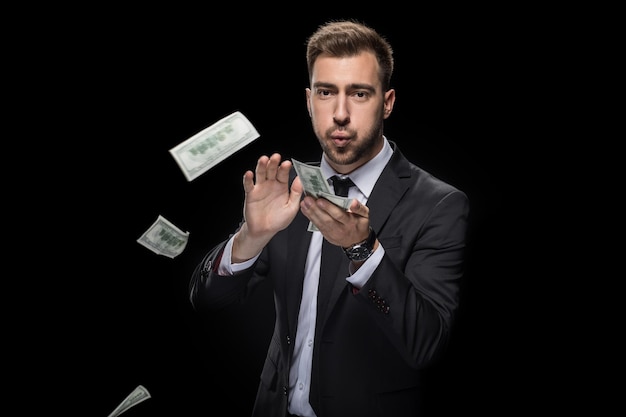 Handsome rich businessman throwing dollar banknotes isolated on black