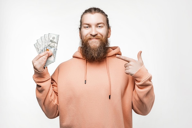 Handsome scandinavian happy man holding dollar currency money in his hands on gray background Guy with ginger hairstyle and beard in a sweatshirt The concept of money salary finance investment